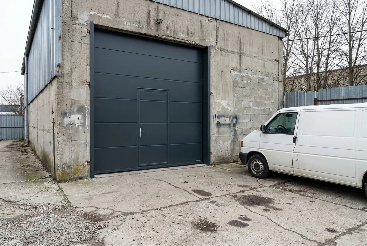 Façade d'atelier avec une porte sectionnelle industrielle gris anthracite fermée et un portillon piéton intégré dans le tablier