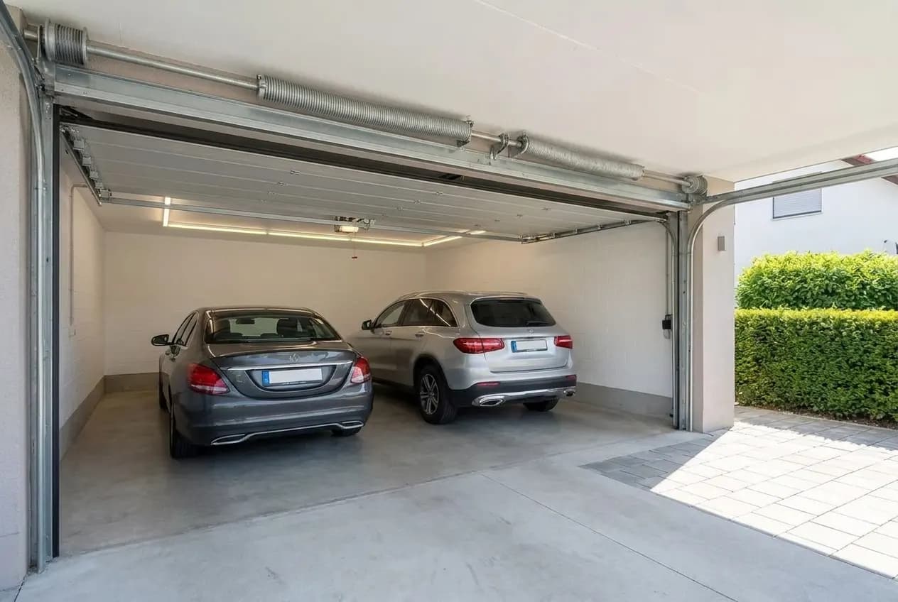 Porte de garage sectionnelle d’environ 5 m de large fermant un garage pour deux voitures, vue de trois quarts