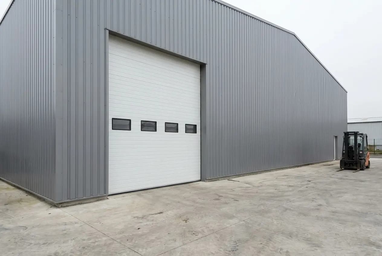 Entrepôt en bardage gris avec une grande porte sectionnelle industrielle blanche à rangée de hublots, fermée