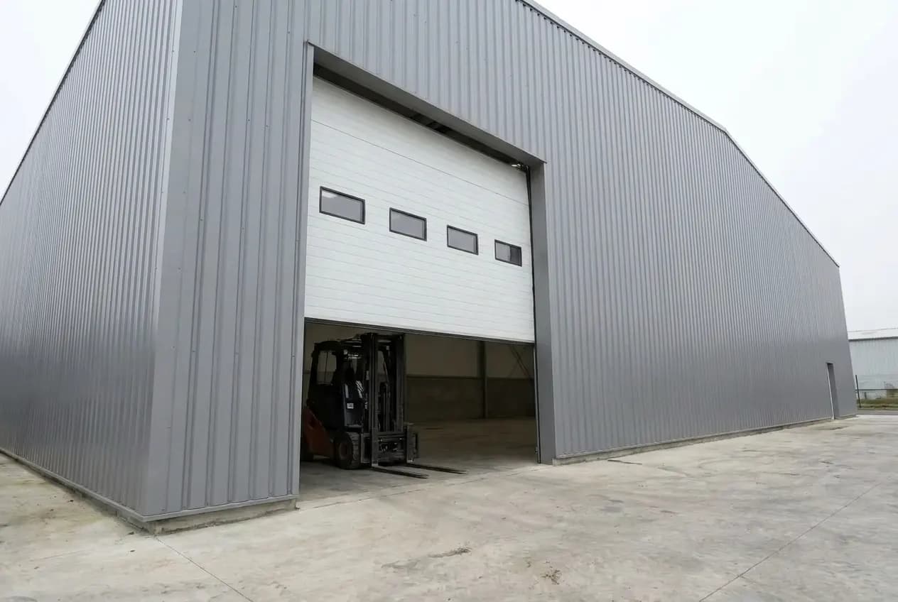 Porte sectionnelle industrielle à demi ouverte, un chariot élévateur à l’intérieur